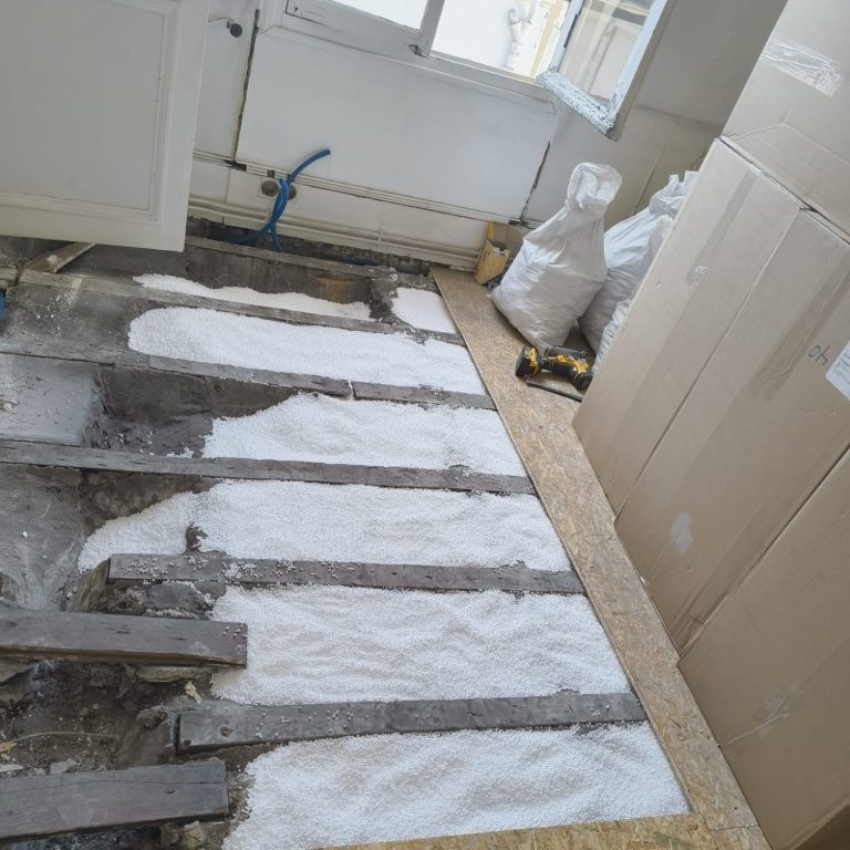 Billes de polystyrène M1 Isolation – PolyXpansion® Sol en cours de rénovation, avec des poutres et de la poudre sur le sol.